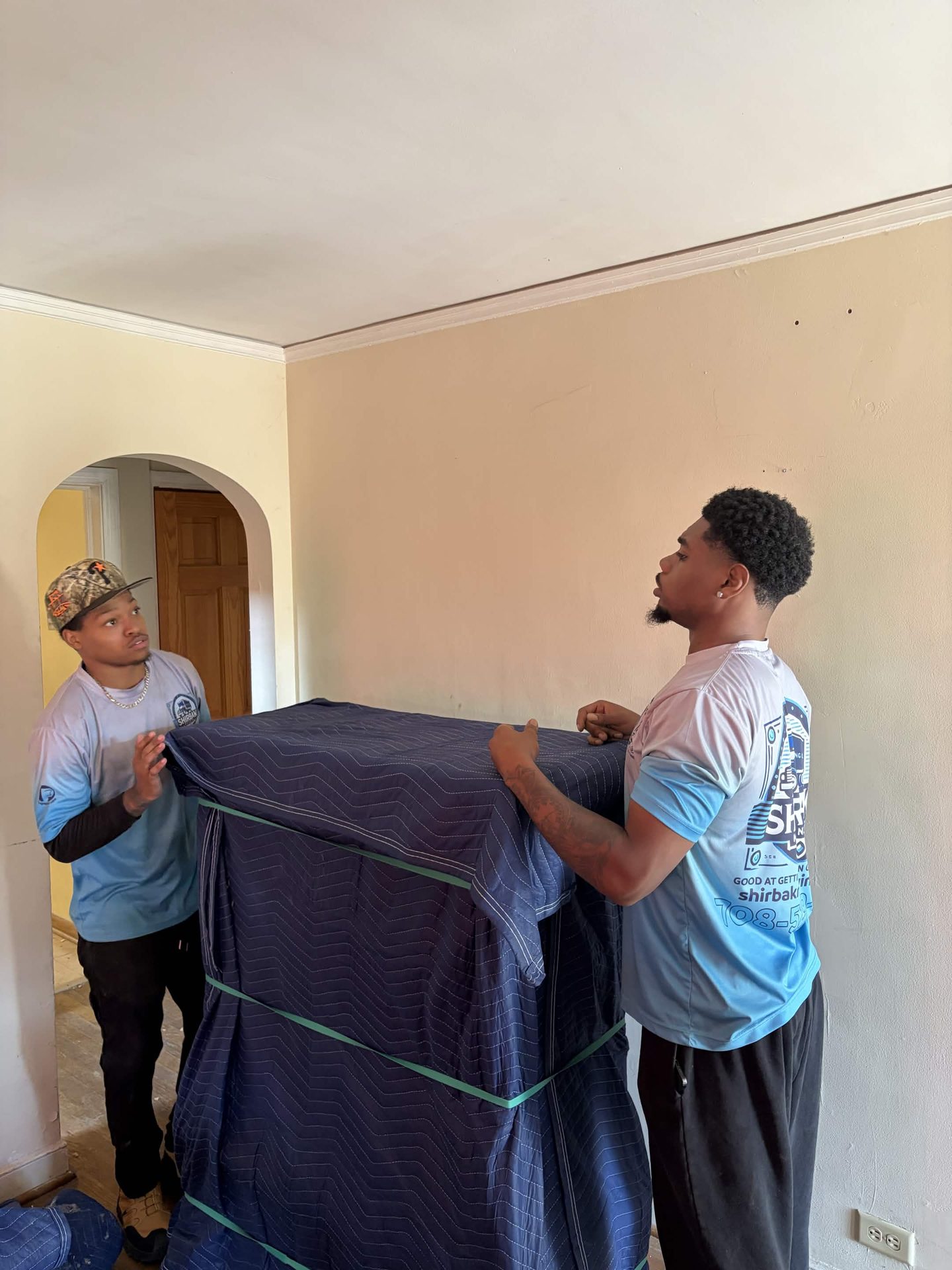 ShirBak movers carry a blanket-wrapped piece of furniture inside a home.