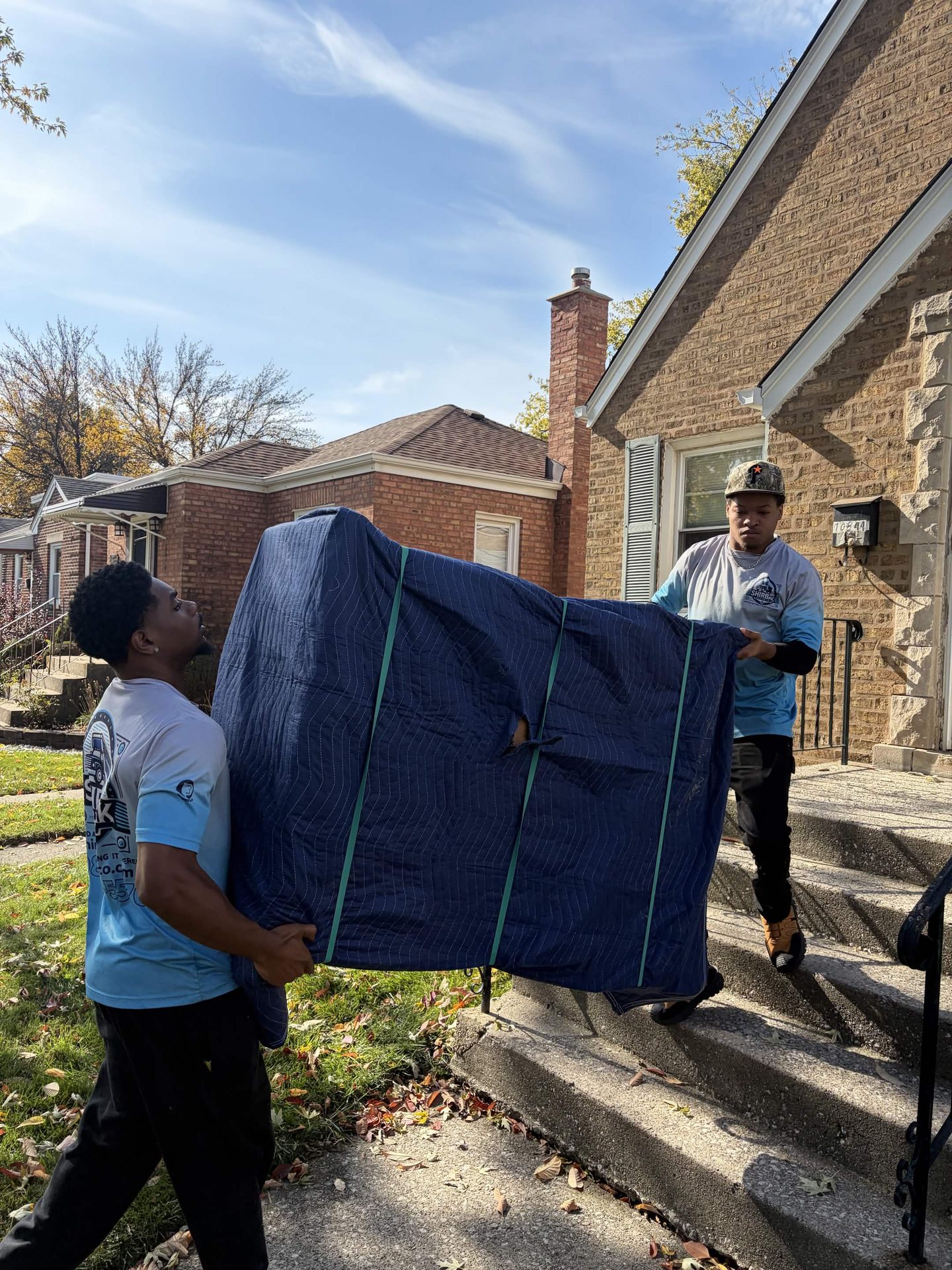 ShirBak movers carry blanket-wrapped furniture down steps.