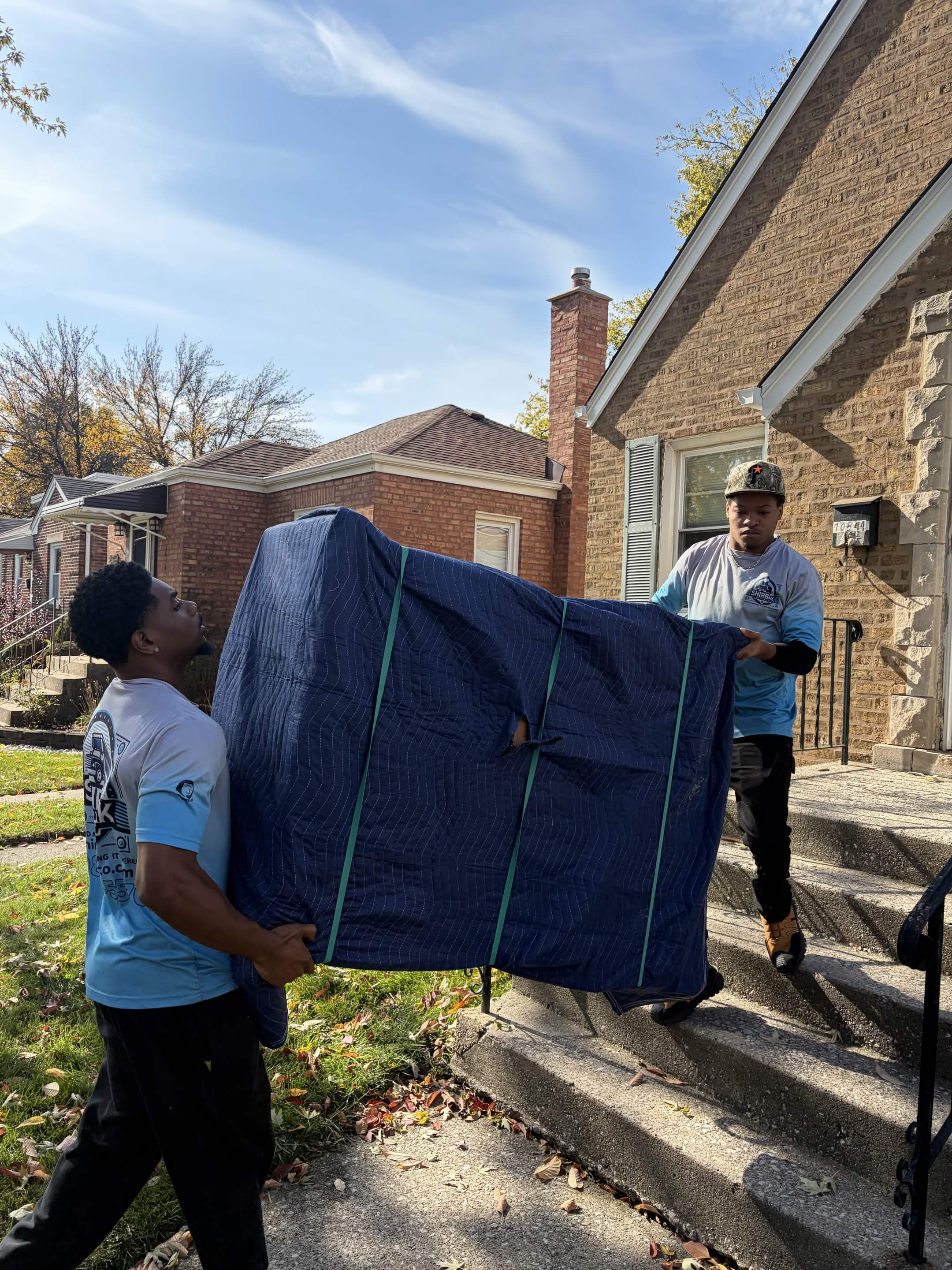 ShirBak movers carrying a wrapped piece of furniture outside a home.